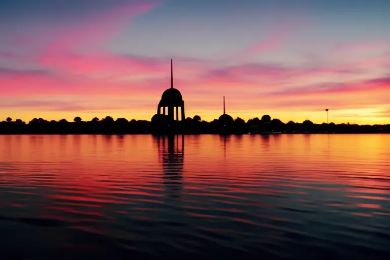 A serene and picturesque landscape featuring the silhouette of a towering structure against a vibrant sunset sky.