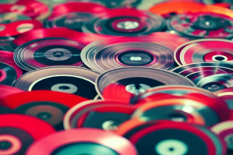 A colorful display of vinyl records arranged in a circular pattern, with a blurred background of abstract shapes and vibrant colors.